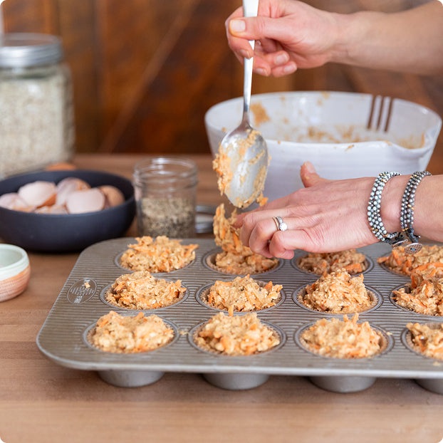 Superhero Muffins Founder Elyse Kopecky filling a muffin tin with a mixture using a spoon on a wooden table.