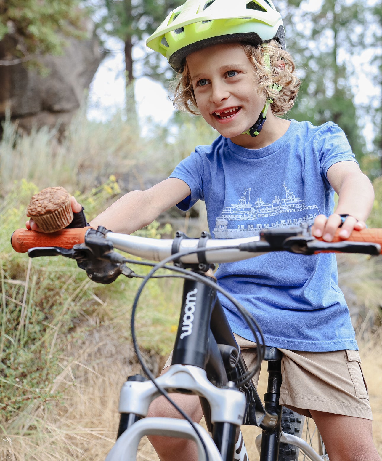 Young boy on a bike holding a Superhero Muffin in the woods