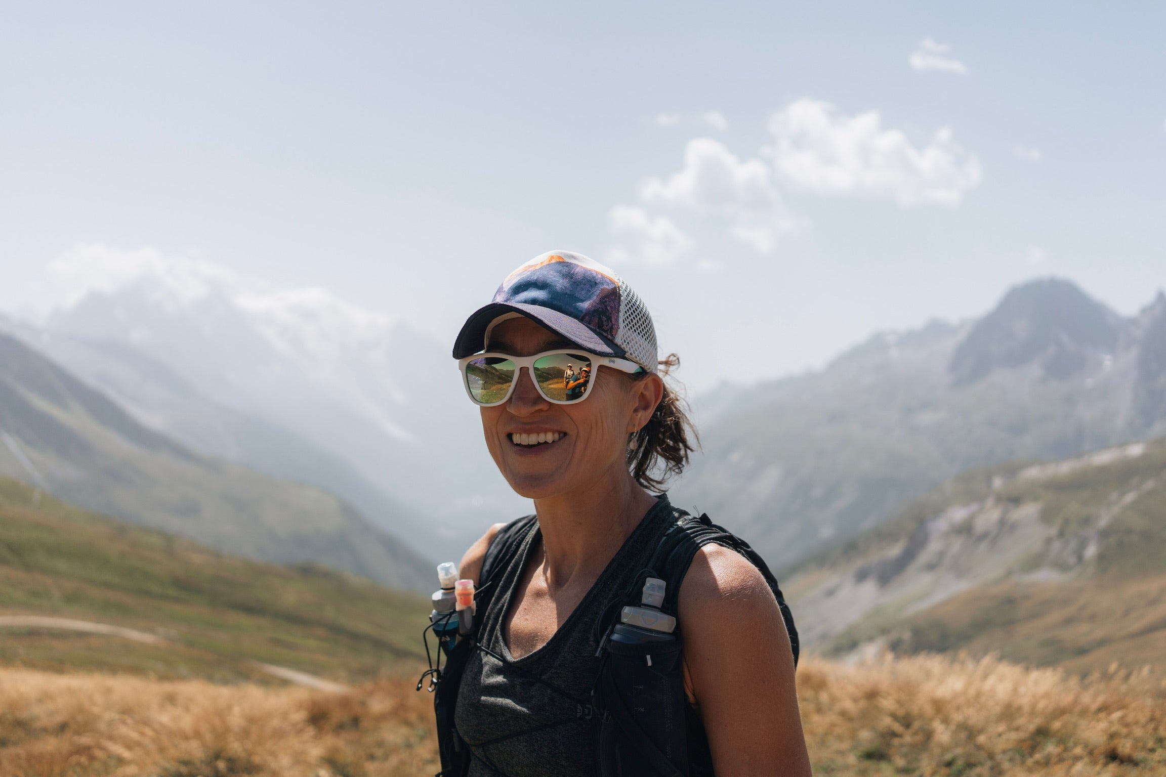 Superhero Muffins customer Amy Cantor wearing a running vest, sunglasses, and hat with mountains in the background.